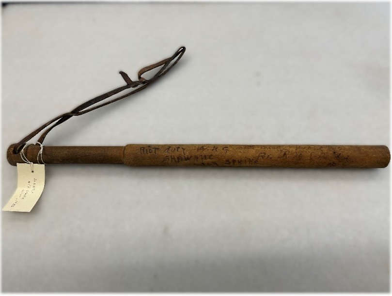 A wooden baton, or night stick with a leather hand strap.