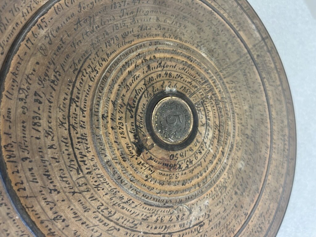A wooden disk with a coin embedded at the center and writing in concentric circles covering the surface.