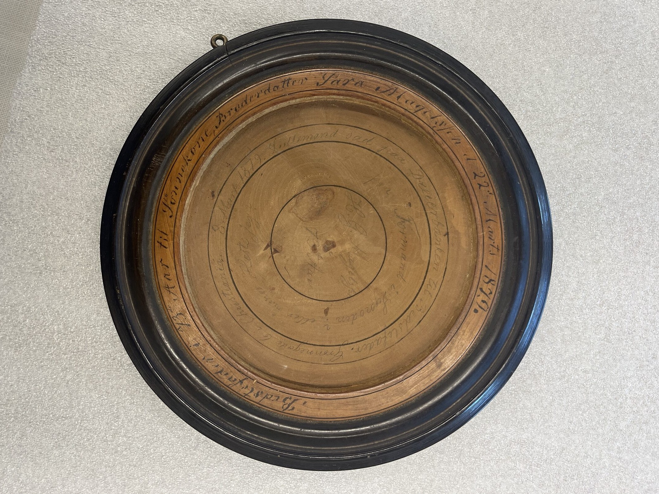 A wooden disk with a dark molden edge, hand script, and painted concentric circles.