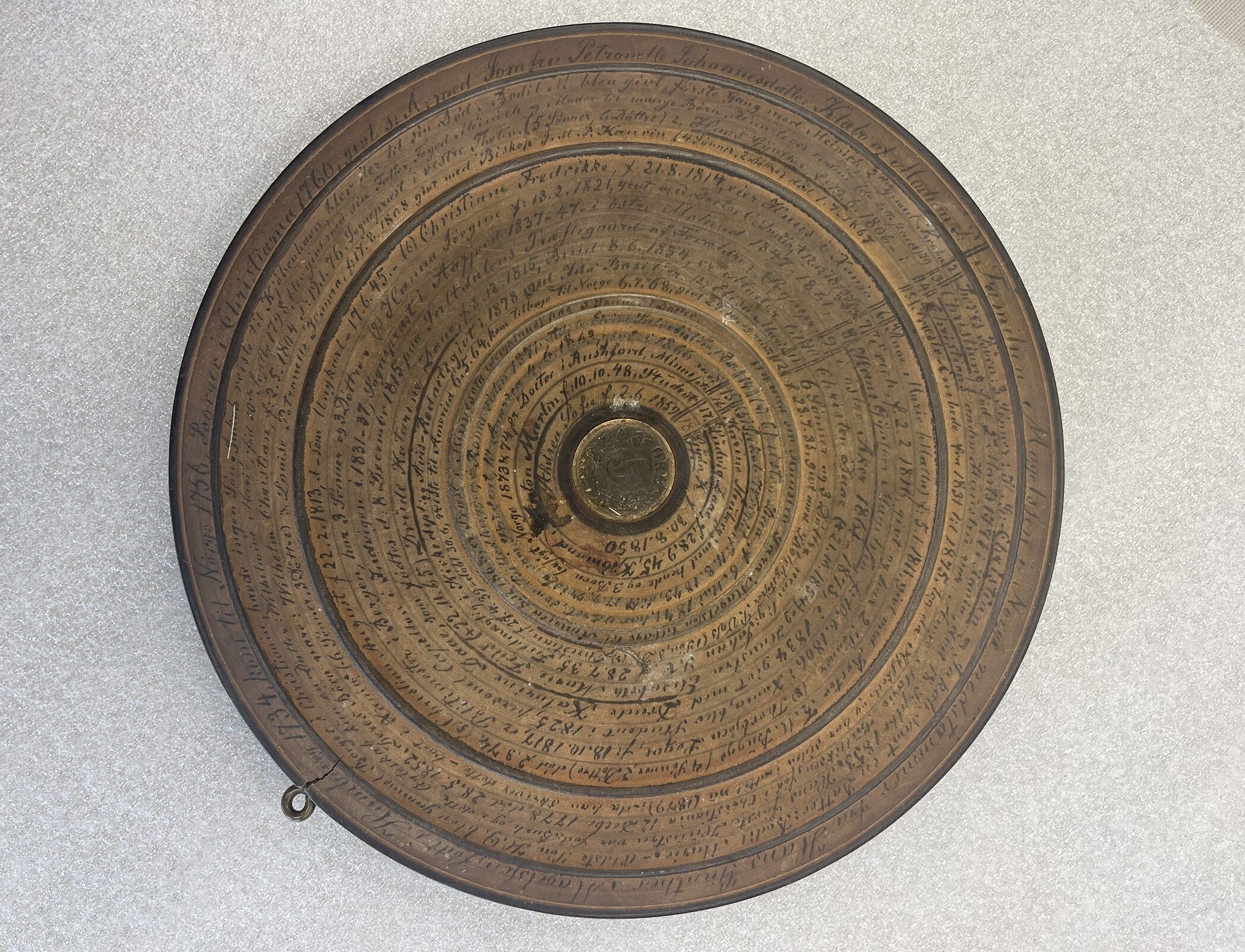 A wooden disk with a coin embedded at the center and writing in concentric circles covering the surface.