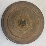 A wooden disk with a coin embedded at the center and writing in concentric circles covering the surface.