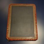 Image of a slate tablet with wooden ruled edges bound with leather.