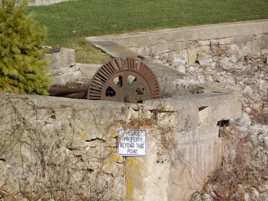 Photograph of a rusted power wheel surrounded by a concrete retaining wall.