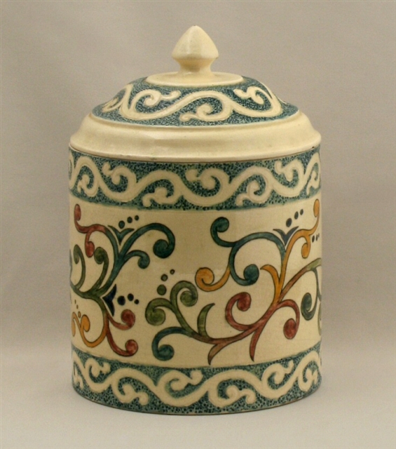 Hand-painted lidded jar. Shaped like a can with a slightly domed lid with finial. The base is cream color, and the painted ornament is of green, red, yellow, and blue vines.