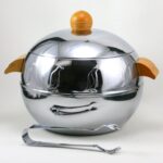 Image of the penguin server, a round aluminum object with wooden handles and repeating molded penguin reliefs around the top.