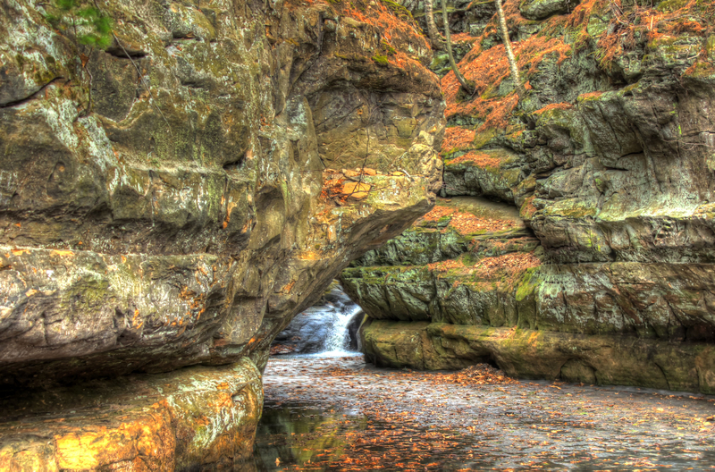 A serene waterfall flows through a narrow canyon, flanked by sandstone bluffs