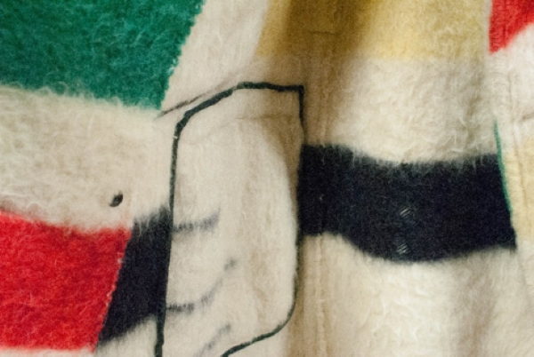 Detail photograph of the interior of a coat made from a woolen point blanket showing black stitching.