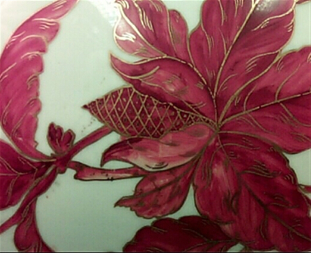 Detail of the hand-painting on ceramic. The design is of a fuchsia flower with gold detailing on a light green background.