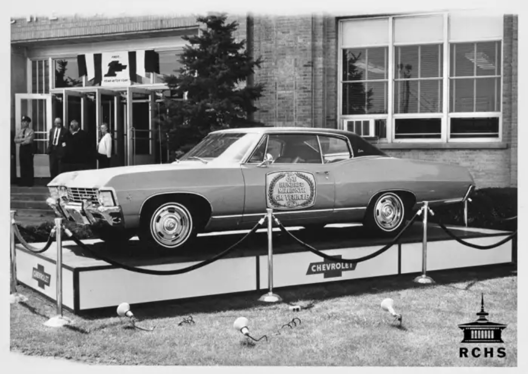 A black and white photograph of a car on a platform in front of a building.