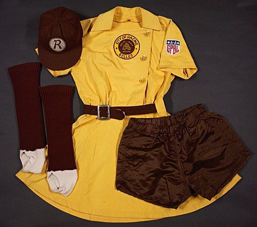 A Racine Belles uniform. Yellow dress with team and league patch and brown belt. Brown short bloomers, brown stirrup socks, and a brown baseball cap with a logo (in off-white) of an R in a circle.