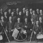 A group photo showing a gathering of men behind an American and a Swiss flag