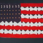 A multi-medium artwork resembling the American flag. The white stripes are made of padded bras. In the field of blue, instead of stars, there are round foam "pills" arranged to resemble a package of contraceptive pills.