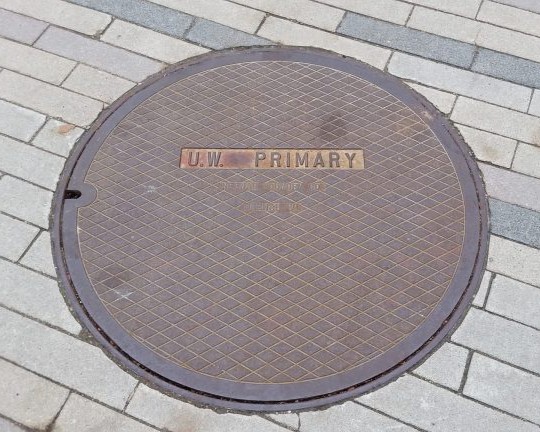 A manhole cover with diamond pattern. In relief it reads, "U.W. Primary."