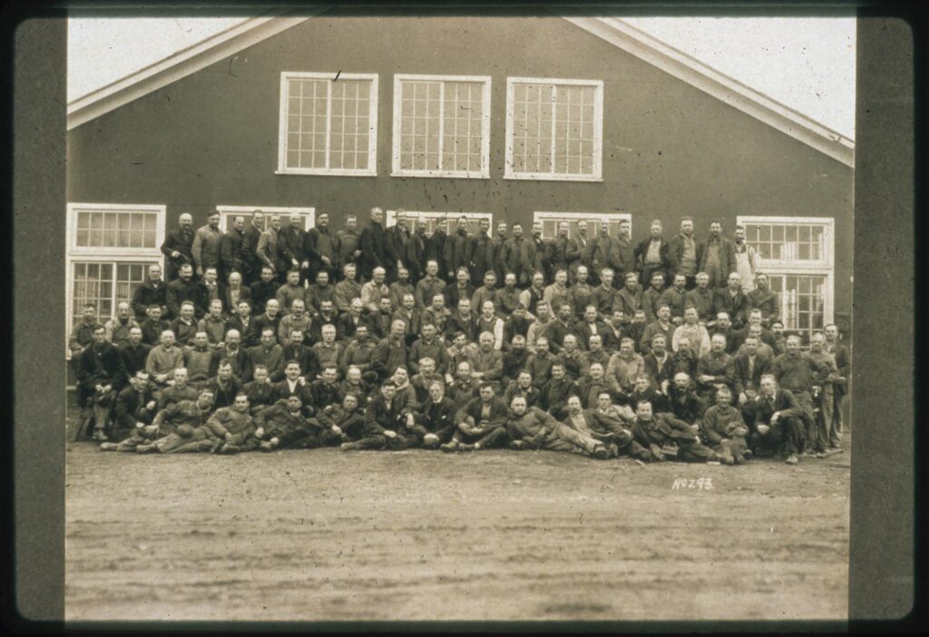 A large group of men posed before a shop building.