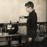 School-age boy cranking the handle of a butterfat testing machine.