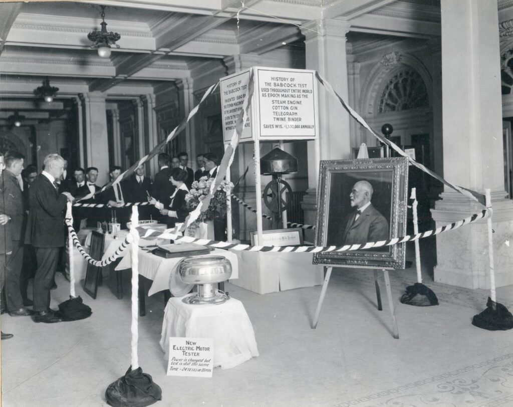 Scene of an exhibition in the Wisconsin State Historical Society with various machines representing the history of the Babcock Test and a painted portrait of Stephen Babcock.