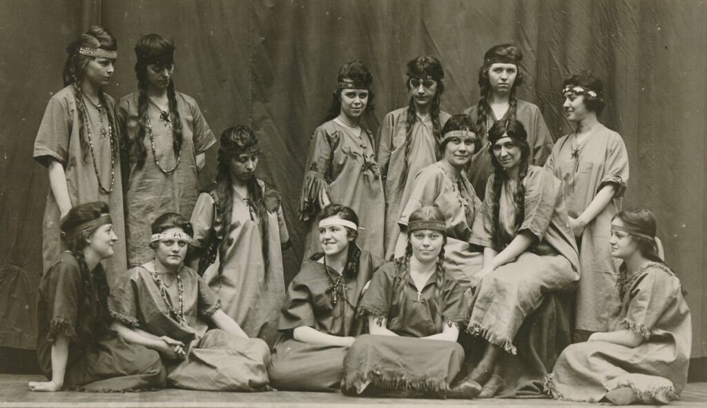 A posed studio photograph of a group of young women dressed in stereotypical Native American costumes.