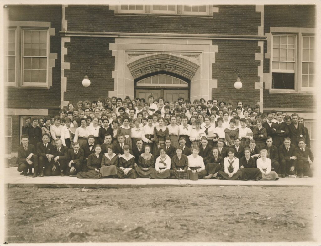 A posed photograph of a large group of students in front of a college hall.