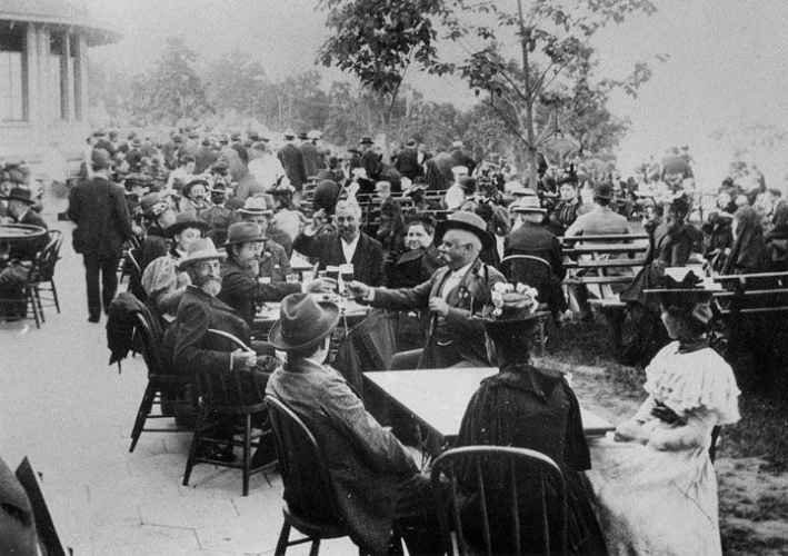 A crowd of men and women sit outdoors at tables and benches.