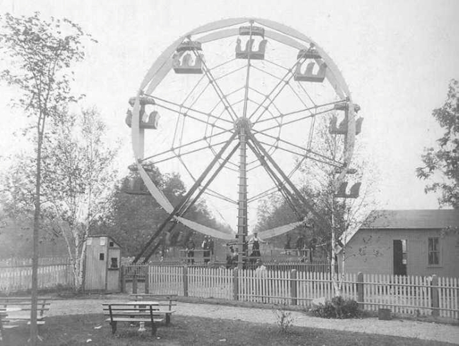 A black-and-white photograph of people posed before a Ferris Wheel.