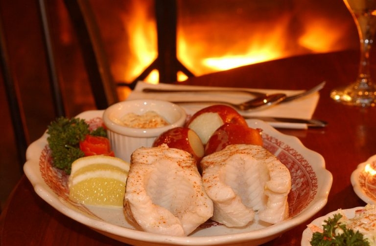 A plate of food: whitefish, boiled potatoes, coleslaw, and lemon wedges.