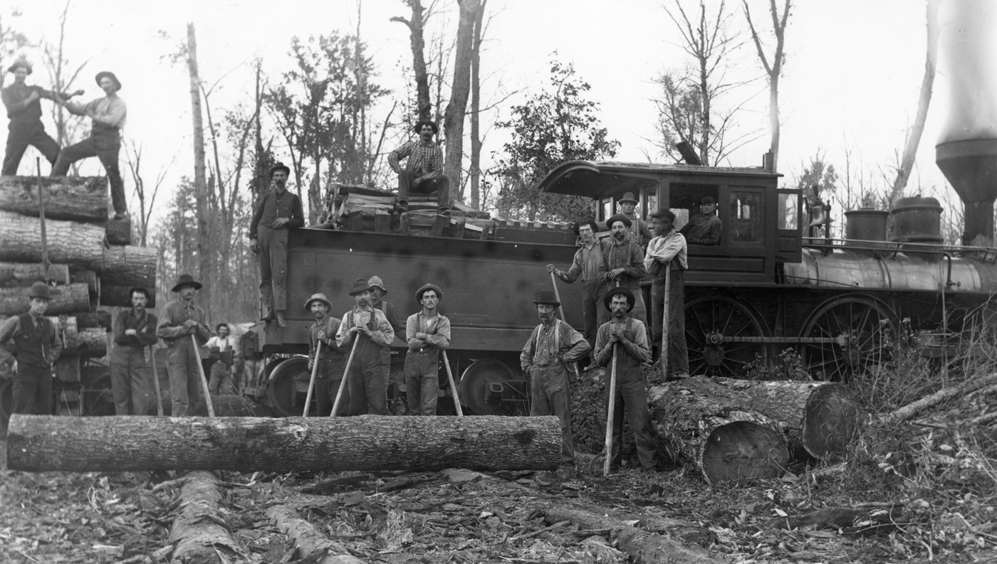 A logging crew of the Upham Lumber Company, posed with logs and tools in front of the company’s locomotive.