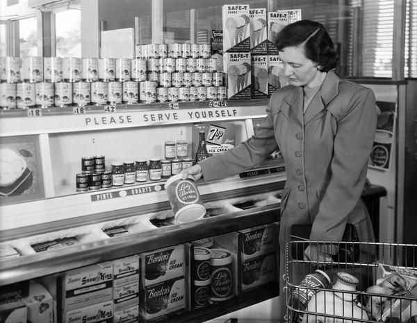 A woman in a long coat chooses a container of Lady Borden brand ice cream from a cooler in a grocery store.