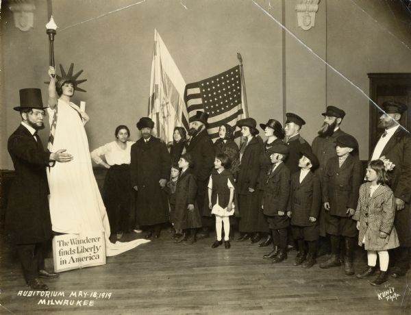 Cast portrait of an Americanzation pageant. Performers are largely in European style costumes, at left a man is dressed as Abraham Lincoln, and he stands next to an actor dressed as the Statue of Liberty.