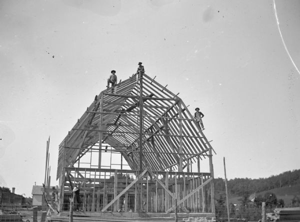 Four men pose with the framework of a barn.