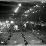 A black and white image of the shop floor of a factory showing workers posing with machines.