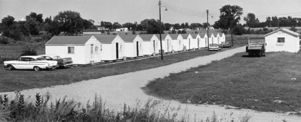A line of small identical buildings line an unpaved road.