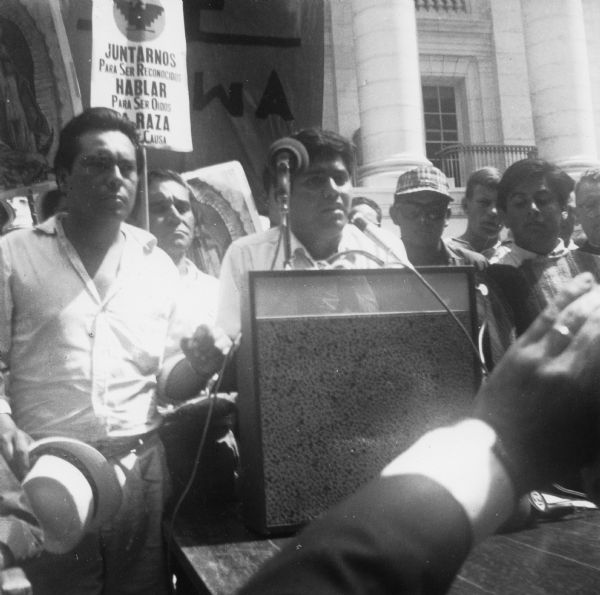 Jesus Salas stands at a podium addressing a crowd in front of the Wisconsin Capitol.