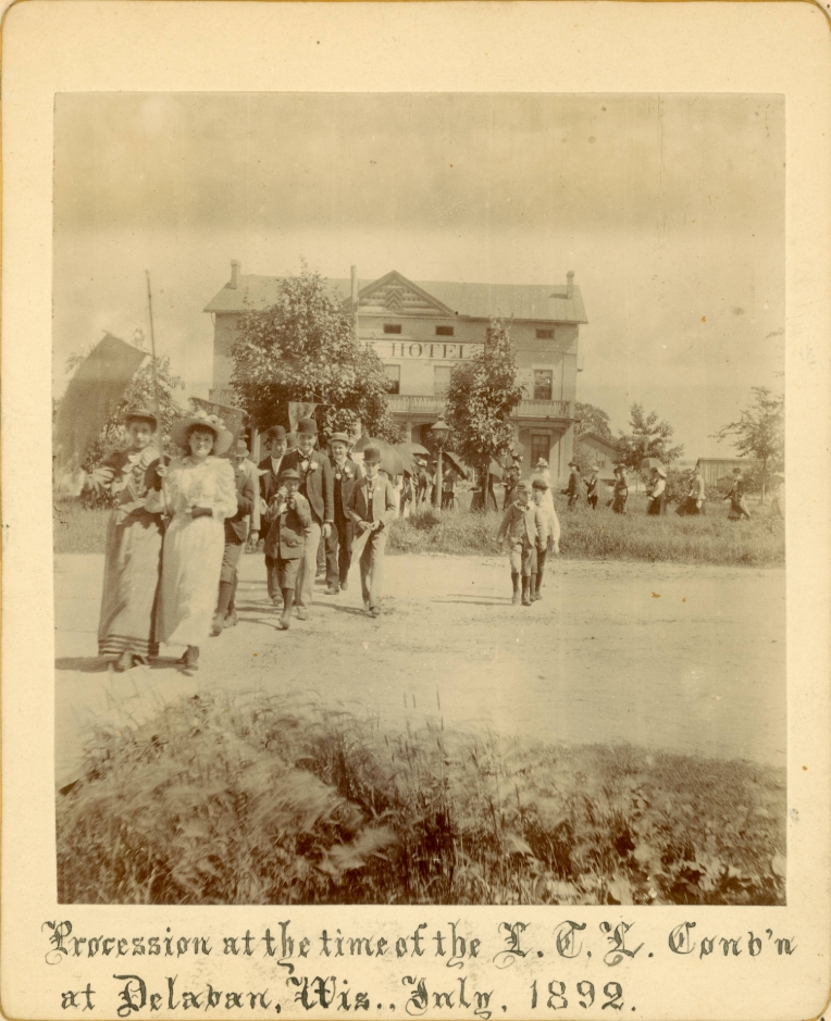 A photograph of a temperance procession, about 50 people walking toward the camera. Caption reads, "Process at the time of the L.T.L. Convention at Delavan, Wisc. July 1892.