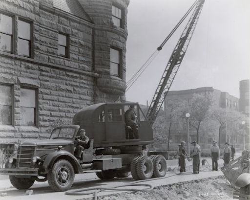 A photograph of a crane on the back of a large truck with three workers behind.
