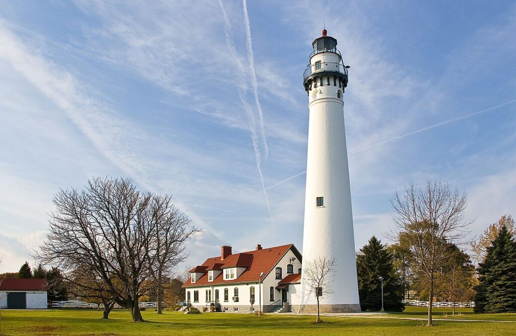 Photograph of the Wind Point Lighthouse and keepers house. The lighthouse towers over the house. The tower, constructed of brick, stuccoed, and painted white, is round and has an observation deck that encircles the lantern.