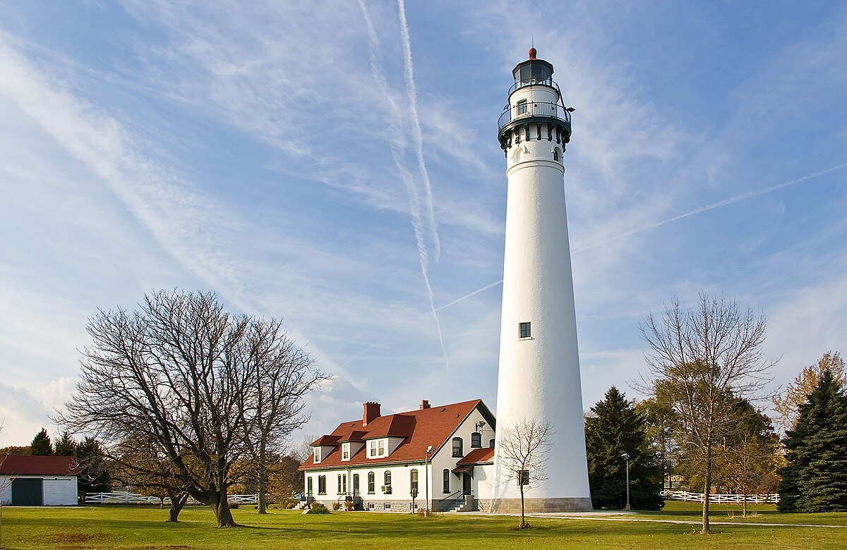 Photograph of the Wind Point Lighthouse and keepers house. The lighthouse towers over the house. The tower, constructed of brick, stuccoed, and painted white, is round and has an observation deck that encircles the lantern.