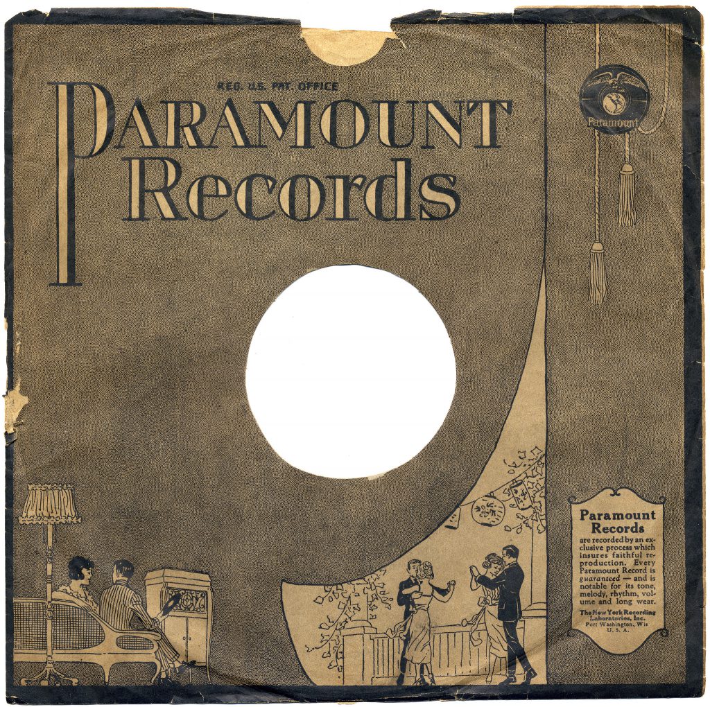A paper record sleeve from the 1920s. This features the company name "Paramount Records" in large print, and illustrations of a man and woman sitting on a sofa next to a phonograph cabinet with a record in hand, and another illustration of two couples dancing on a patio.