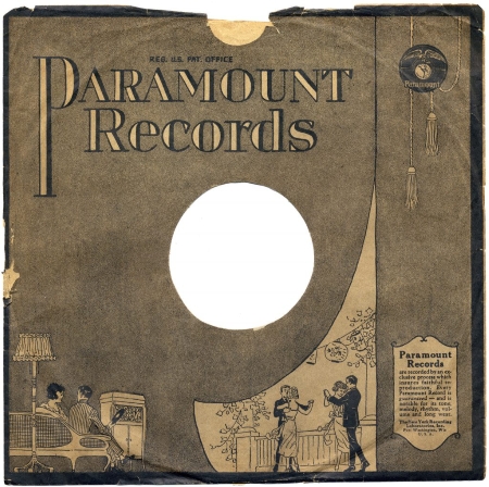 A paper record sleeve from the 1920s. This features the company name "Paramount Records" in large print, and illustrations of a man and woman sitting on a sofa next to a phonograph cabinet with a record in hand, and another illustration of two couples dancing on a patio.