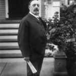 Photo portrait of William Horlick in front of his house holding a rolled newspaper.