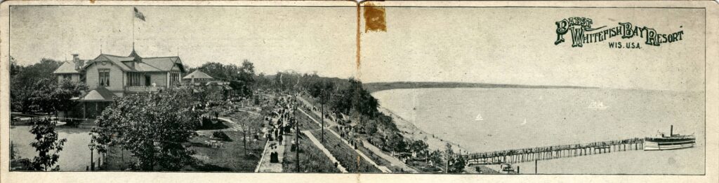 Panoramic elevated view of the Victorian-era Pabst Whitefish Bay Resort overlooking Lake Michigan with people walking up the numerous paths leading to the resort’s entrance. A pier extends into the lake and at the end is a steamboat.