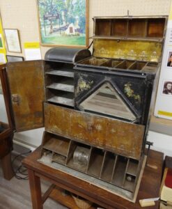 A metal cabinet with various compartments, shelves, and doors. Some are labeled with stenciled and painted kitchen staples like "flour" and "sugar"
