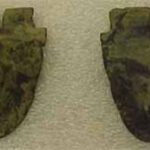 Two small masks made of copper with faint detailing of faces.