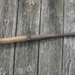 Photograph of a bark spud. A spade-shaped tool with long wooden handle.