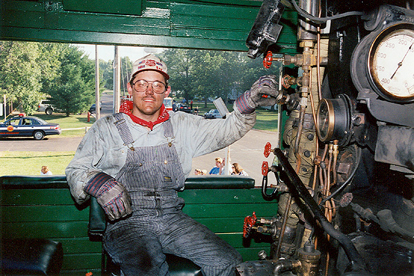 Photograph of a man dressed in striped overalls operating the steam engine.