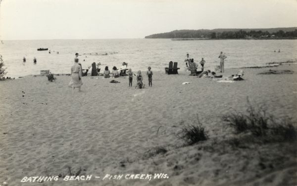 A black-and-white image of figures on a sandy beach and bathing in shallow water.