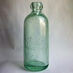 A green glass bottle with molded relief lettering that reads, “C CASSEL WHITE FISH BAY WIS”