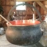 Copper cheese kettle, blackened on the exterior, cauldron-like with steel handle.