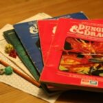 A collection of Dungeons & Dragons components, including books, grid paper, a pencil, and dice, arrayed on a table.