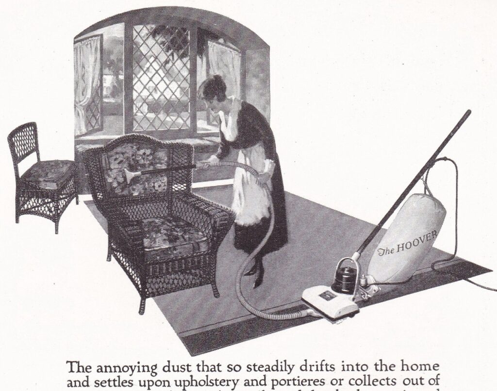 A ca. 1920 advertisement for a Hoover brand vacuum cleaner. It shows a woman, in maid uniform using a hose attachment for a upright vacuum cleaner to dust a wicker chair.