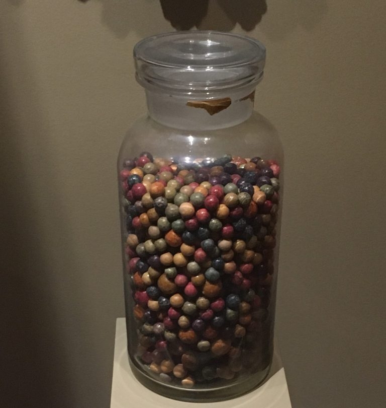 A lidded glass jar almost full with many different colored marbles.